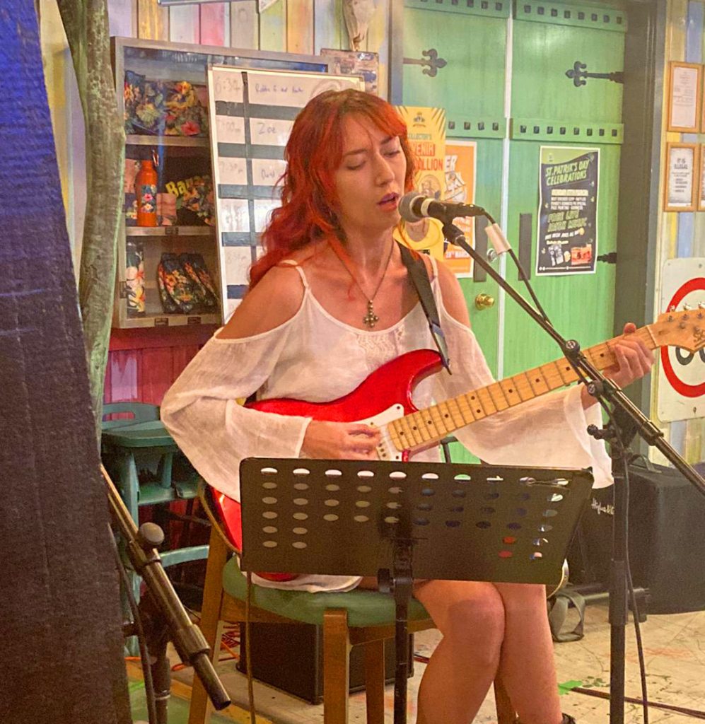 A woman singing and playing guitar at open mic night